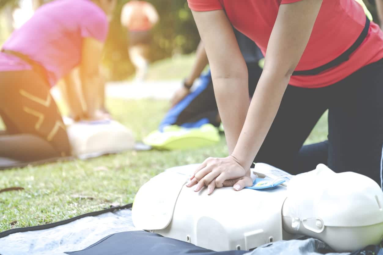Asian female or runner woman training CPR demonstrating class in park by put hands and interlock finger over CPR doll give chest compression. First aid training for heart attack people or lifesaver.